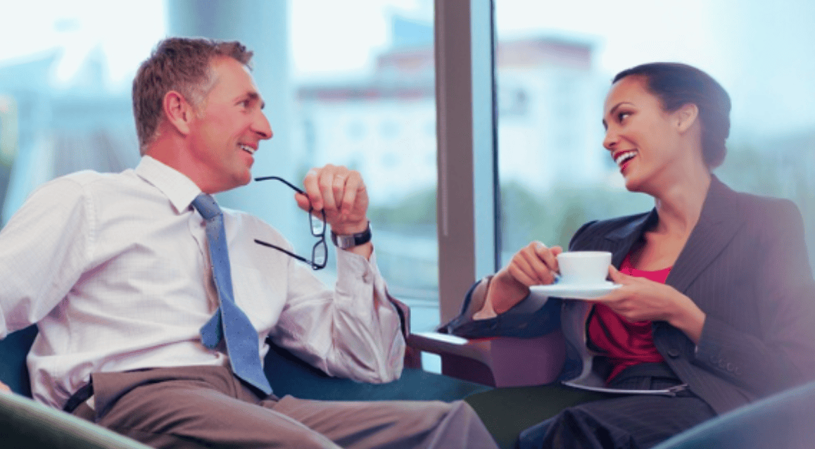 A male and a female executive at work smiling and standing back to back before a Connor Executive English course